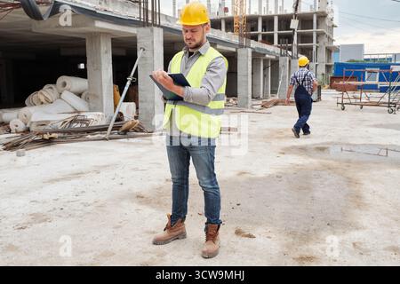 Site engineer with a safety equipment walking and carrying blueprints ...