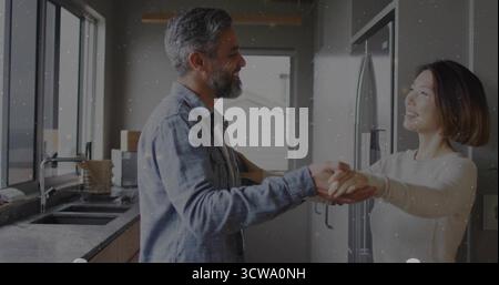 Dancing mature couple holding hands in modern home kitchen, with stainless steel refrigerator Stock Photo