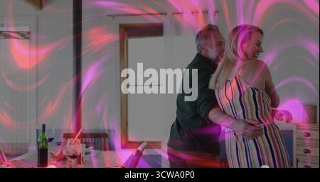 Dancing mature couple embracing in kitchen, with wine bottle, wine glasses and laptop, copy space Stock Photo