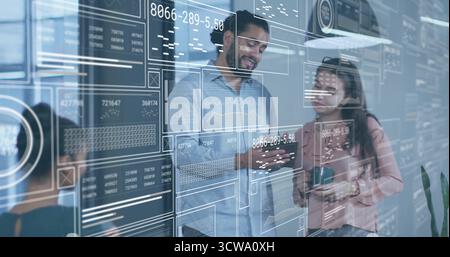 Pointing businessman in blue shirt holding smartphone at glass wall in office, with digital charts Stock Photo