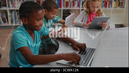 Sitting three students using laptop and tablets at white study table in library, with bookshelves Stock Photo
