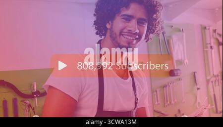 Smiling man wearing white shirt and apron, holding tool in garage with pegboard, subscriber overlay Stock Photo