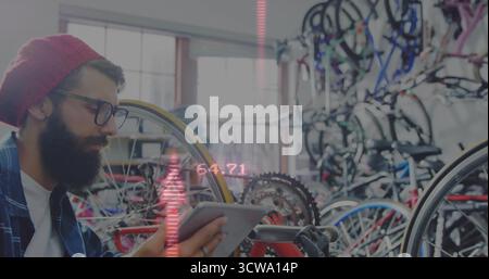 Adjusting bearded mechanic wearing red cap in bicycle repair shop consulting tablet, copy space Stock Photo