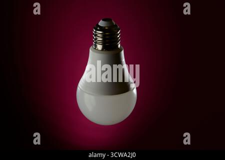 Studio shot of LED light bulb positioned against dark magenta gradient background. Represents creative idea, energy conservation and technology advanc Stock Photo
