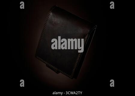 Horizontal studio image of black leather wallet lying on dark red background. Simple still life concept with moody lighting and elegant texture emphas Stock Photo