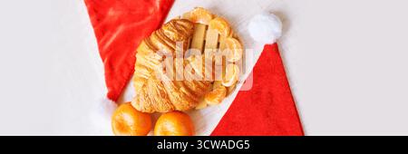 Festive breakfast with croissants and oranges on santa hats background. Stock Photo
