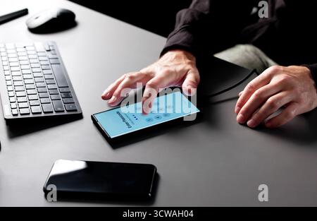 Man In Balaclava Hacking Into Smartphone To Steal Sensitive Data. Stock Photo