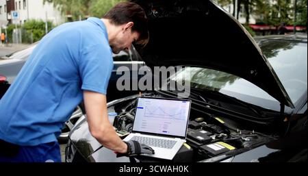 Skilled Senior Mechanic Using Laptop To Diagnose Car Engine Issues. Stock Photo