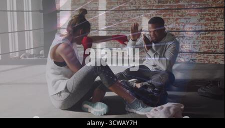 Trainee punching with red hand wraps and trainer holding pads in boxing ring, with bag, ropes Stock Photo