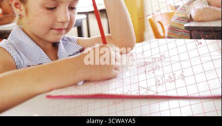 Writing math equations boy sitting at school desk on graph paper in classroom, with red pencil Stock Photo