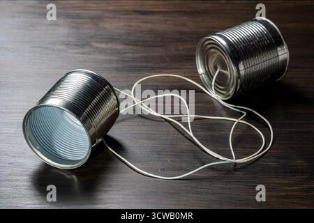 Tin cans as telephones connected by string on a wooden background, close up, communication concept Stock Photo
