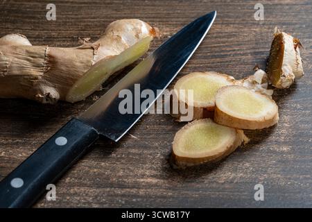 Cutting ginger root into pieces with a knife on a wooden cutting board, close up Stock Photo