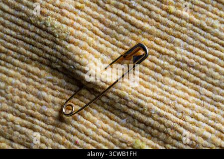 Gold toned safety pin on yellow fabric background, close up. Metal pin in rough textile fabric closed, macro Stock Photo