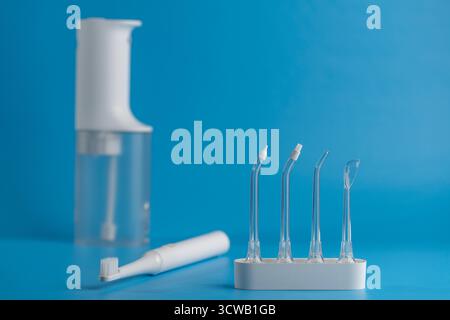 Portable oral irrigator with different attachments and white electric toothbrush on blue background, close up. Dental care, flosser bucal tooth cleane Stock Photo