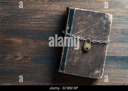 Metal chain and padlock around old book on wooden background, close up, top view. Copy space for text Stock Photo