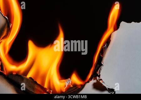 White paper burning on a black background, close up. Paper burns, smoke and turns into ashes. Fire and paper Stock Photo