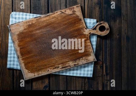 Empty cutting board over towel on wooden kitchen table, top view, close up, copy space Stock Photo