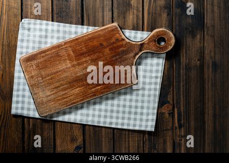 Empty cutting board over towel on wooden kitchen table, top view, close up, copy space Stock Photo