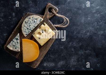 Set of different cheeses on wooden cutting board on a black background, close up, top view, copy space . Various types of cheese Stock Photo