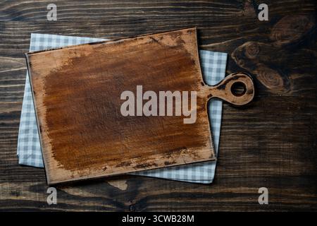 Empty cutting board over towel on wooden kitchen table, top view, close up, copy space Stock Photo