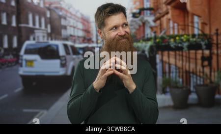 Young caucasian man with reddish beard and fingertips touching on urban street under daylight; confidence. Stock Photo