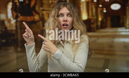 Woman raises her hand pointing toward hall displays while her blonde hair frames a young excited figure in a museum lobby with intricate architecture. Stock Photo