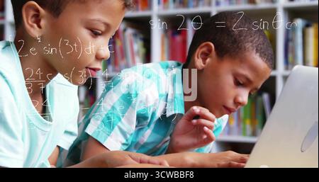 Studying two boys solving math problems in study room, with laptop and bookshelves with books Stock Photo