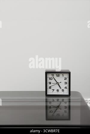 Square alarm clock stands on a black glass table on a white background, copy space Stock Photo
