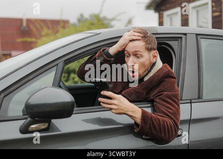 Shocked man sitting inside car with smartphone in hand. Stock Photo