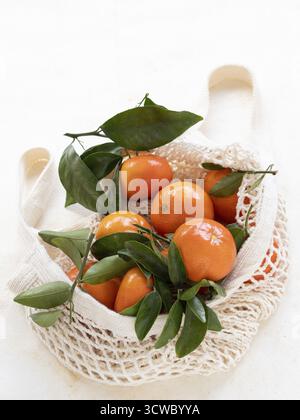 Ripe tangerines with green leaves inside a reusable mesh bag promoting sustainable shopping Stock Photo