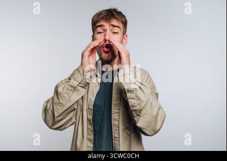 portrait of young man passionately shouts with expression, using his hands to convey strong emotions on white background Stock Photo