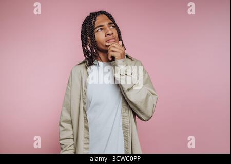 portrait of young thoughtful man with a pensive look contemplates while gazing upward on pink background Stock Photo