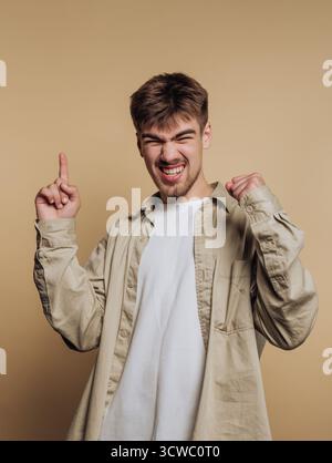 portrait of young enthusiastic man raises his finger in excitement, capturing a vibrant moment of joy on beige background Stock Photo