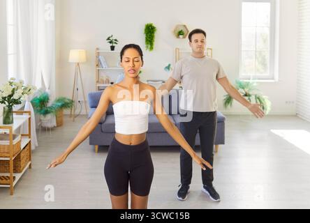 Couple practicing yoga workout and meditation at home, breathing with hands up Stock Photo