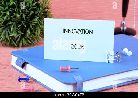Business vision for the future year 2026 is shown with Innovation printed on a white paper. It is secured to a Blue notebook with a clip and surrounde Stock Photo