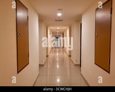 Long Indoor Hallway With Two Wooden Doors On Each Side Reflective Floor And Overhead Lights Stock Photo