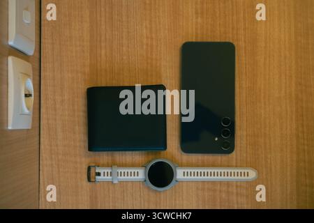 Overhead View Of Black Leather Wallet Smartphone And Smartwatch On Wooden Surface With White Wall Socket Stock Photo