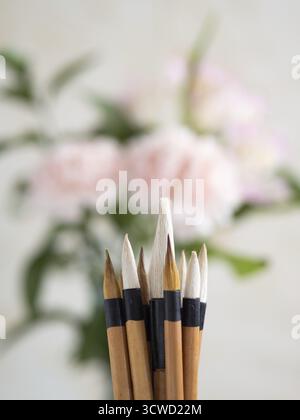 Close-up of chinese calligraphy brushes with pink carnations blurred in the background, creating a tranquil artistic scene Stock Photo