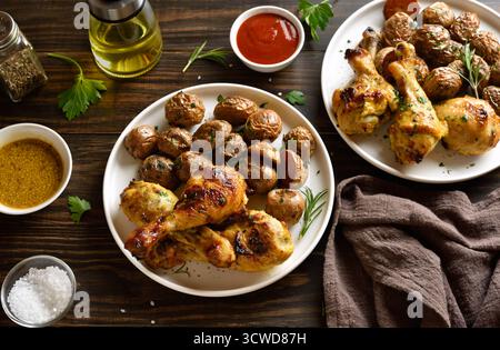 Grilled chicken drumsticks with roasted potatoes on white plate on brown wooden table. Stock Photo