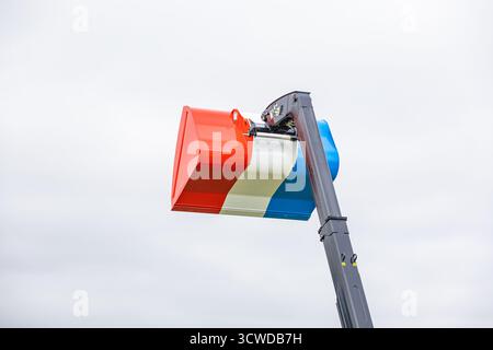 Construction excavator bucket decorated with red white and blue stripes resembling French national flag against overcast sky Stock Photo