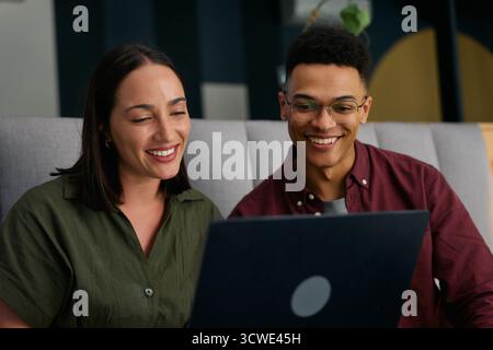 Smiling diverse young business colleagues in smart casual using laptop at desk in office Stock Photo