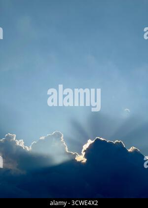 Crepuscular rays branch out from behind a cloud near sunset. Stock Photo