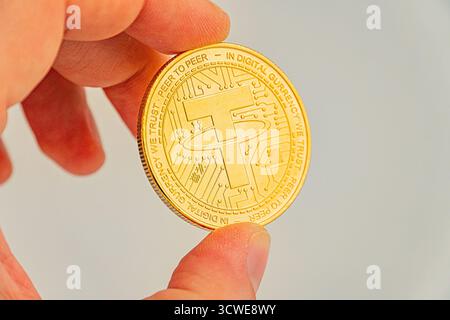 A stock image depicts a person holding a gold Tether coin against a neutral backdrop, symbolizing investment, cryptocurrency, and technological innova Stock Photo