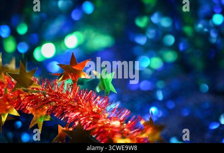 Golden stars on red tinsel over blue sparkling blurred surface with bokeh lights. Stock Photo