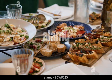 A vibrant close-up shot showcases a lavish antipasto spread with bruschetta, mixed salads, and various olives on a white linen-covered table, evoking Stock Photo