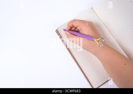 Hand writing in brown leather notebook with purple pen on isolated white background. Person holding pen over open notebook. Writing, productivity Stock Photo