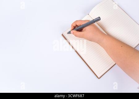 Hand writing in brown leather notebook with purple pen on isolated white background. Person holding pen over open notebook. Writing, productivity Stock Photo
