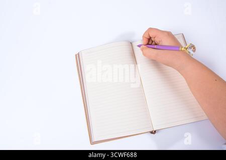 Hand writing in brown leather notebook with purple pen on isolated white background. Person holding pen over open notebook. Writing, productivity Stock Photo