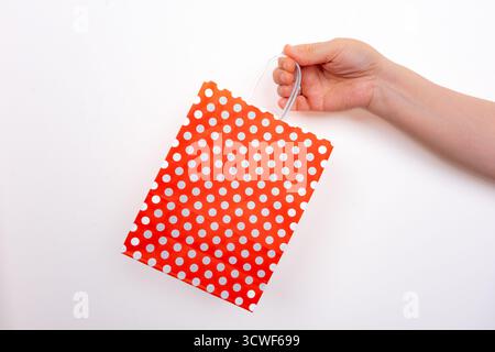 Hand holding red polka dot gift bag on isolated white background. Person gripping red dotted shopping bag. Gift and celebration concept Stock Photo