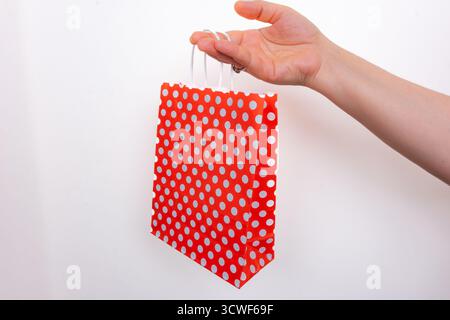Hand holding red polka dot gift bag on isolated white background. Person gripping red dotted shopping bag. Gift and celebration concept Stock Photo